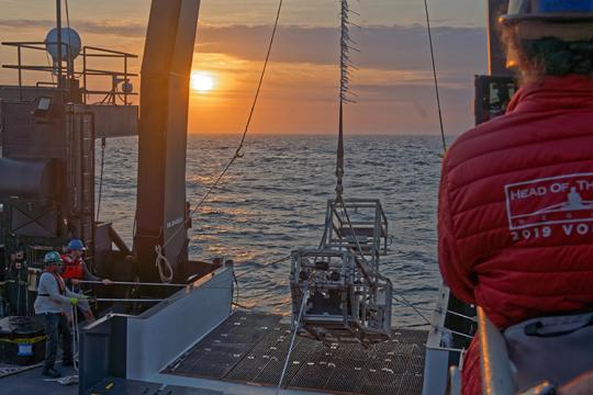 The HabCam going over the stern of a research vessel with deckhands managing a deployment using cables.
