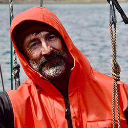 Portrait of scientist wearing an orange jumpsuit with the ocean in the background. 