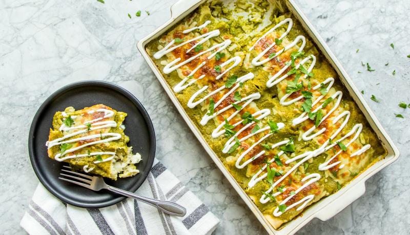 Baking pan of pollock enchiladas next to plated serving with fork.